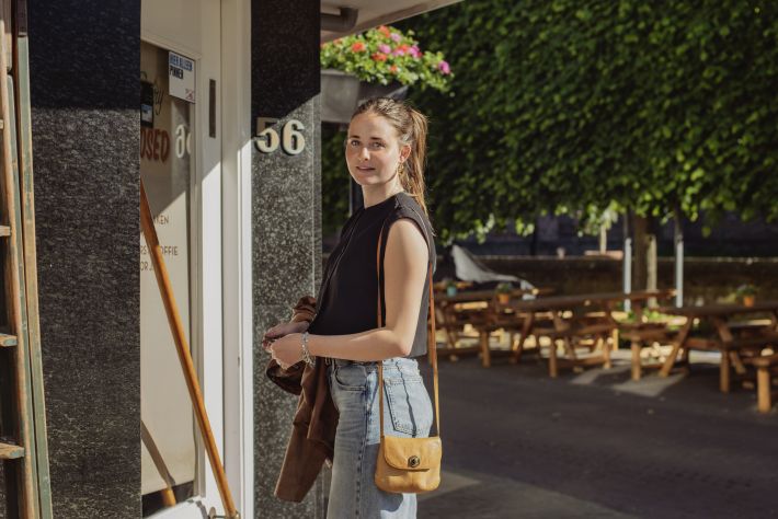Milou staat voor het cafe waar ze werkt en kijkt glimlachend naar de camera